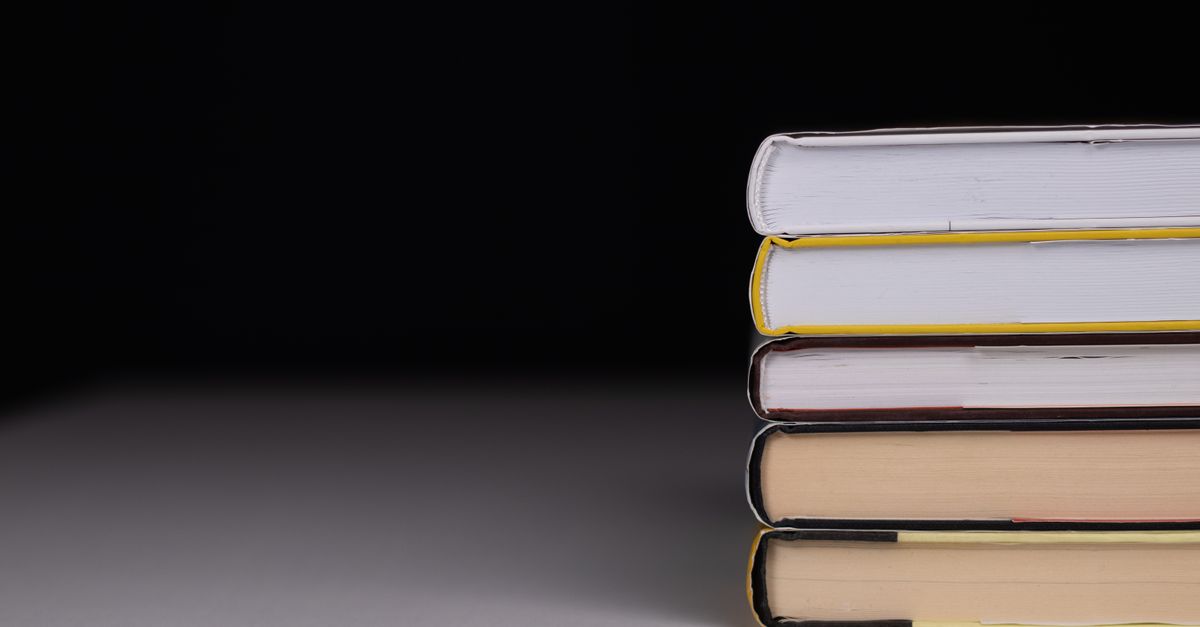 Minimalist stack of hardcover books with a black background and subtle lighting.